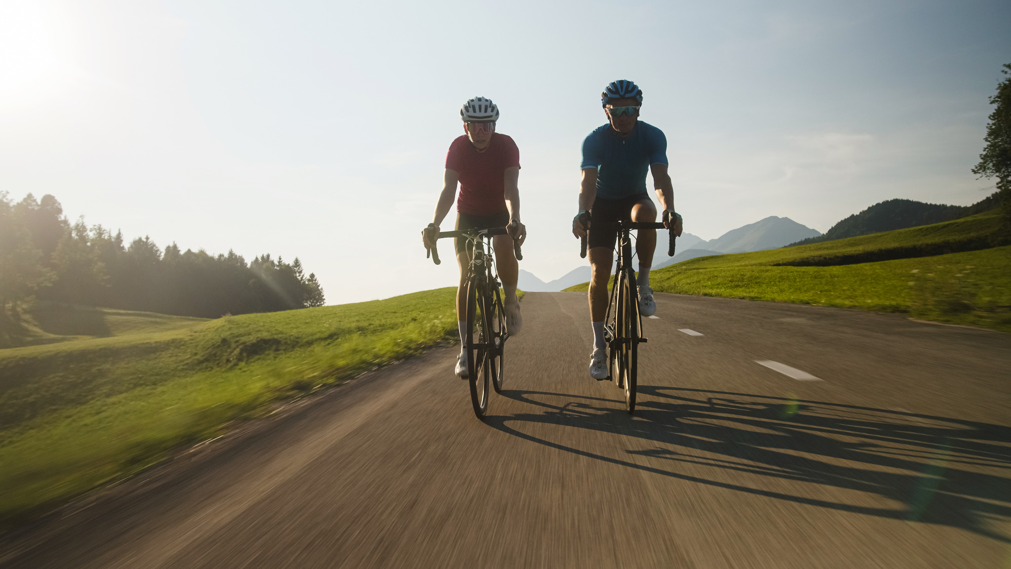 Zwei Personen fahren mit E-Bikes auf einer Landstraße.